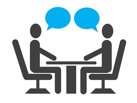 Dos personas sentadas, cada una en un lado de la mesa conversando.