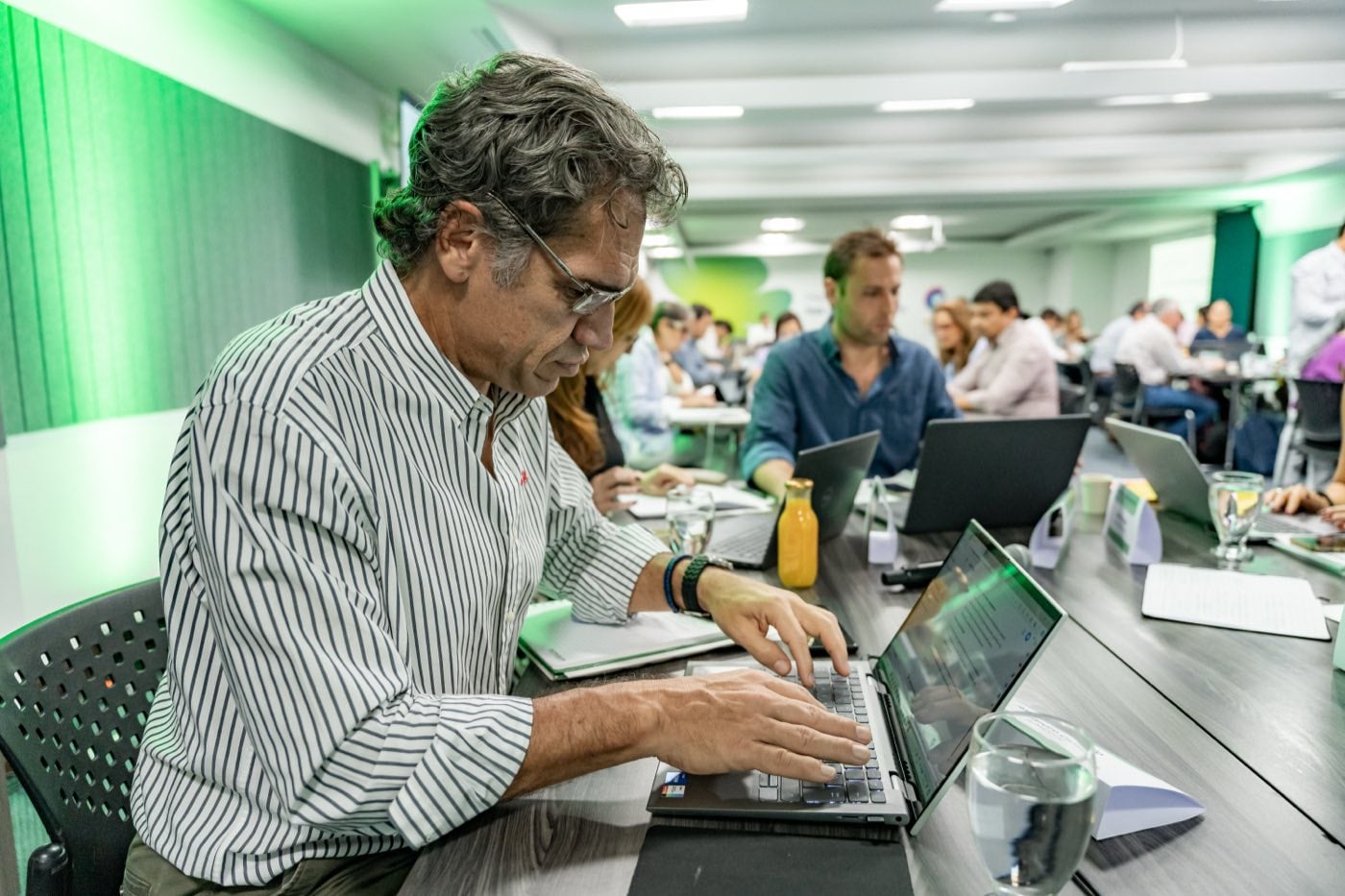 Un directivo trabajando en su laptop durante una sesión del Programa Ejecutivo, con el resto de la cohorte en mesas al fondo