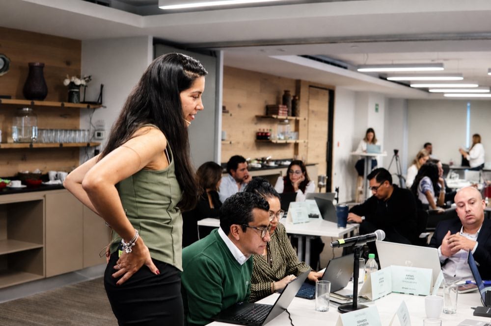 Una instructora de pie conduciendo la sesión junto a participantes que trabajan en sus computadores