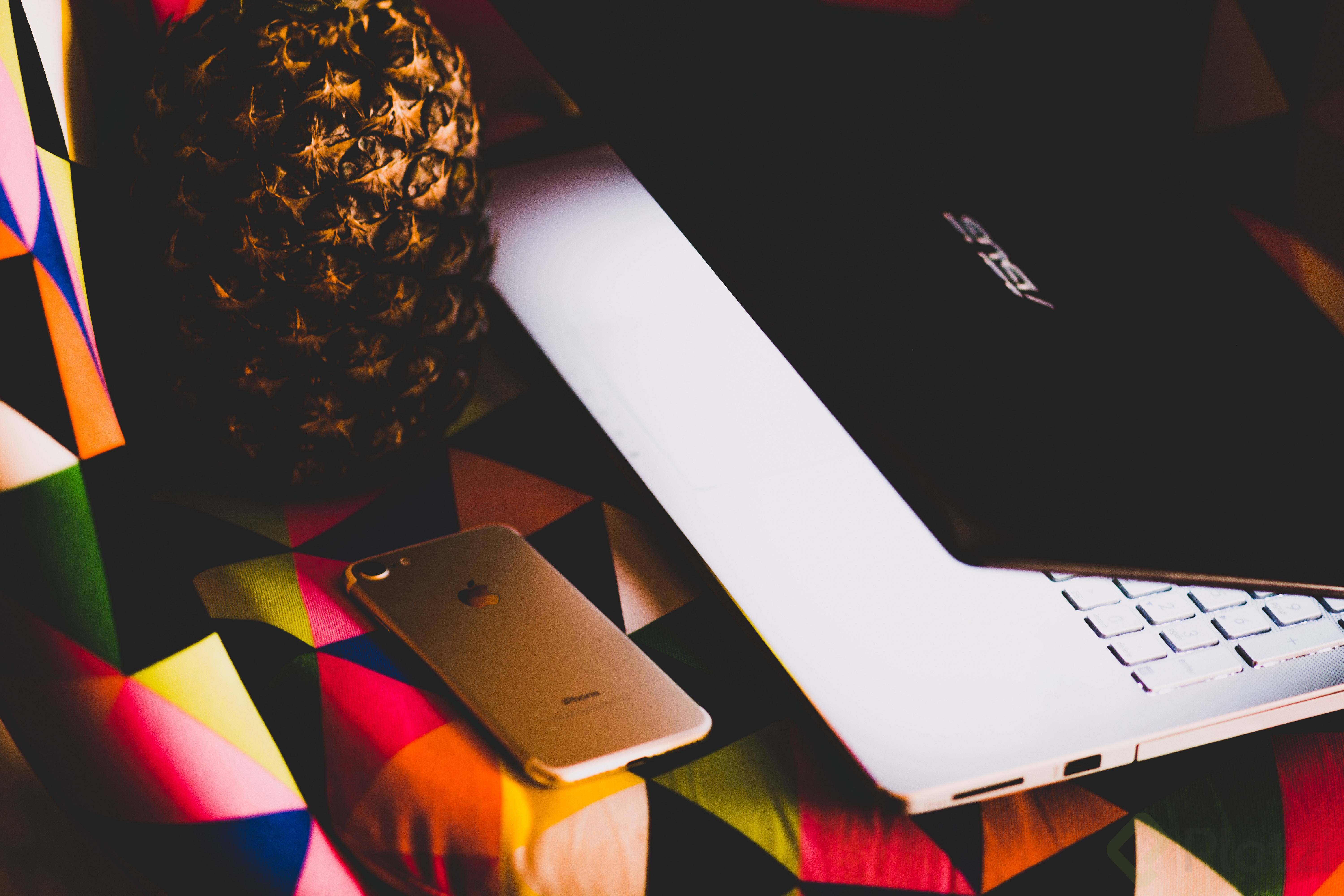 Una piña, un iPhone y una laptop sobre una mesa con un mantel de colores
